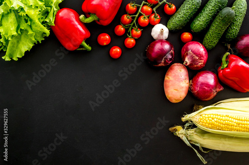 Set of autumn vegetables - potato, cucumber, carrot, greenery - on black background top-down copy space