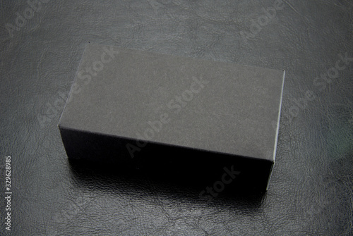 Black, rectangular, paper box matte color on a black leather background. Cardboard package.