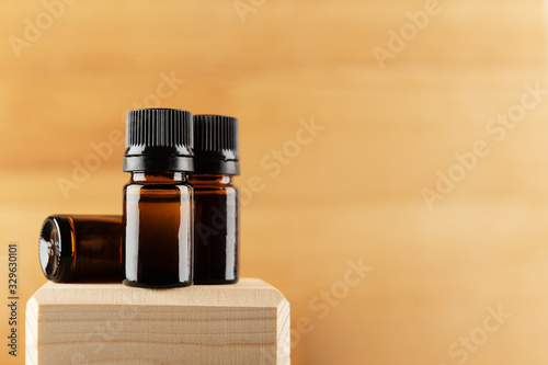 Glass bottles set for aromatherapy, massage oil or essential cosmetics products. Unbranded flacons on on wooden stand isolated on beige backdrop. Copy space in right side. Organic cosmetology concept