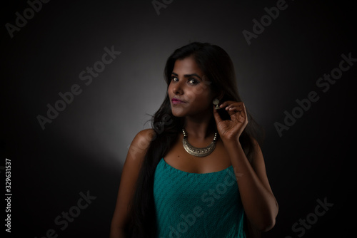 Fashion portrait of young dark skinned Indian/African brunette girl in green western dress and jewelry in front of black copy space studio background. Indian fashion photography.