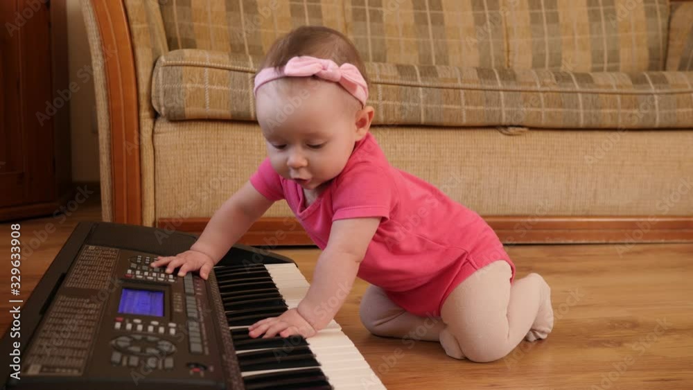 Funny baby toddler playing piano synthesizer crawling the floor at home wearing pink Funny baby toddler playing piano synthesizer crawling the floor at home wearing pink