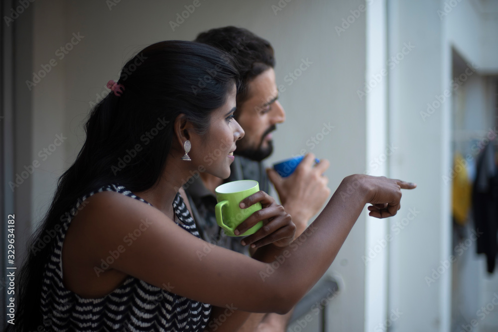 A dark skinned Indian/African girl in western dress and a Kashmiri/European/Arabian man in casual wear spending time with coffee/tea on a balcony in white background. Indian lifestyle. A dark skinned Indian/African girl in western dress and a Kashmiri/European/Arabian man in casual wear spending time with coffee/tea on a balcony in white background. Indian lifestyle.