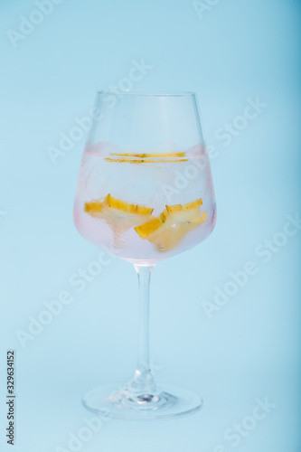 Glass of fresh iced cocktail decorated with starfruit slice on blue background.