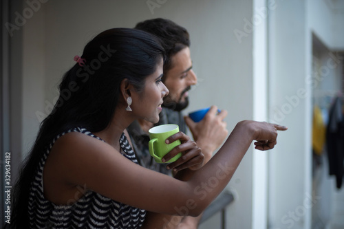 A dark skinned Indian/African girl in western dress and a Kashmiri/European/Arabian man in casual wear spending time with coffee/tea on a balcony in white background. Indian lifestyle.