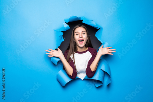 Young pretty woman surprised looking through blue hole in paper wall.