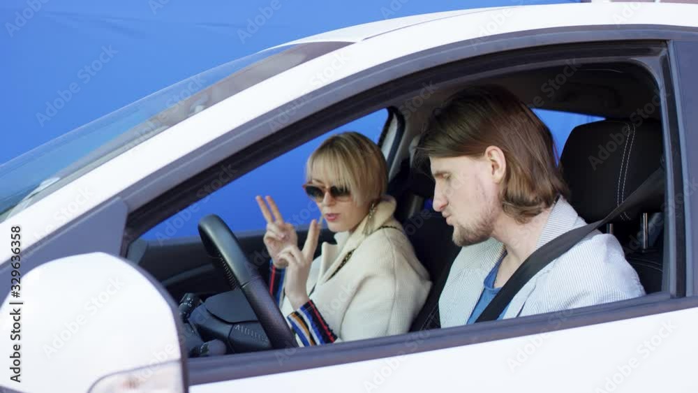 Crazy driver and cheerful passenger are dancing and enjoying music while travelling by car. Brunette man and blonde woman are sitting inside white car with blue chroma key background. Man imagines he Crazy driver and cheerful passenger are dancing and enjoying music while travelling by car. Brunette man and blonde woman are sitting inside white car with blue chroma key background. Man imagines he