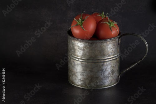Red tomatoes in an iron jug on black background
