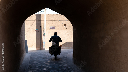 Man on a motorcycle riding in the narrow street of old city Yazd  Iran.