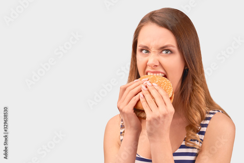 Cute girl quickly eats Burger, wrinkling nose, getting angry, Baring teeth. Wears striped t-shirt, isolated on white background in Studio with space for advertising photo