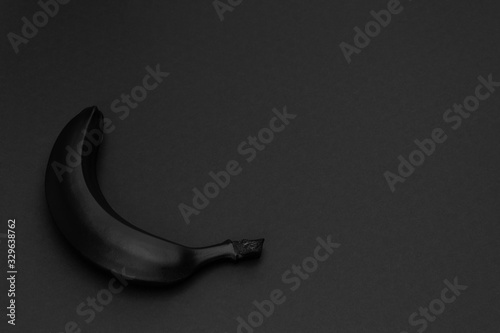 Black banana on the matte black background. Minimal style. Conceptual minimalist black art. Matte surface. Fruit. One. Space for text