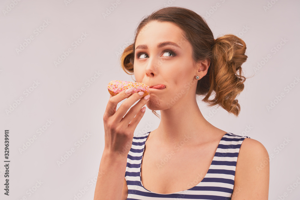 Young attractive woman with stylish hair, a nice smile, holding a bitten donut, taking a bite of the dessert, looks up at Metso . Close-up portrait on a white background. Young attractive woman with stylish hair, a nice smile, holding a bitten donut, taking a bite of the dessert, looks up at Metso . Close-up portrait on a white background.