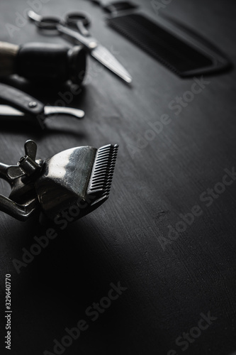 On a black dusty surface are old barber tools. Vintage manual hair clipper comb razor shaving brush shaving brush hairdressing scissors. vertical. black monochrome.