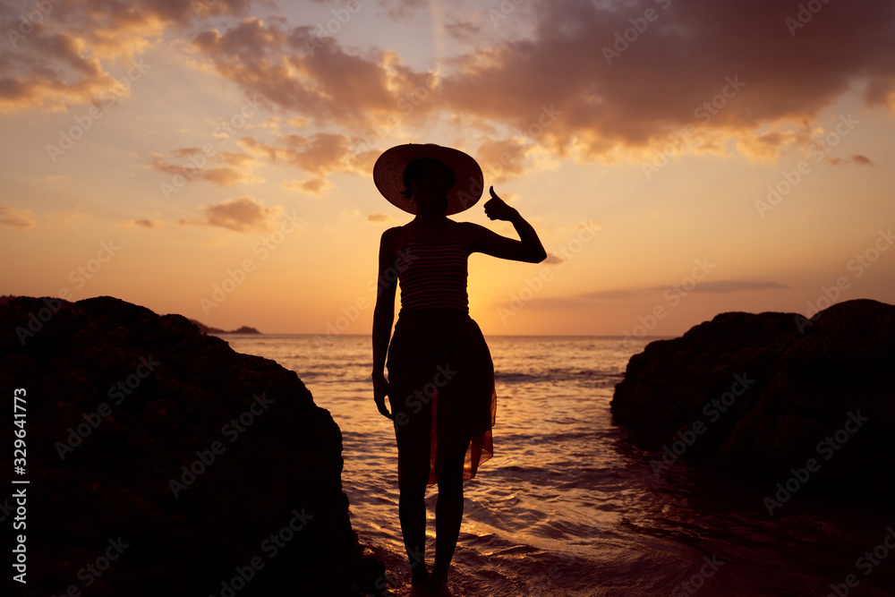 Contrast silhouette of young slender woman against background of Sunny sunset, sea and sandy beach. Warm evening tones. Lady walking on beach in sunset, vacation in city Patong Phuket country Thailand