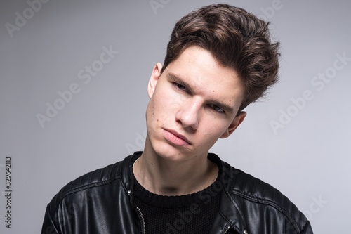 Wide angle. Studio shot. Young caucasian guy model in black clothes posing in the studio. Teenager in Leather Jacket Standing at White Background. young fashion model wearing black coat in studio
