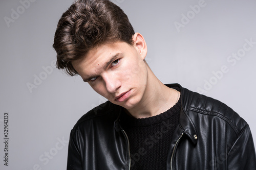 Wide angle. Studio shot. Young caucasian guy model in black clothes posing in the studio. Teenager in Leather Jacket Standing at White Background. young fashion model wearing black coat in studio