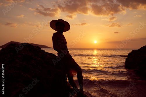 Contrast silhouette of young slender woman against background of Sunny sunset  sea and sandy beach. Warm evening tones. Lady walking on beach in sunset  vacation in city Patong Phuket country Thailand