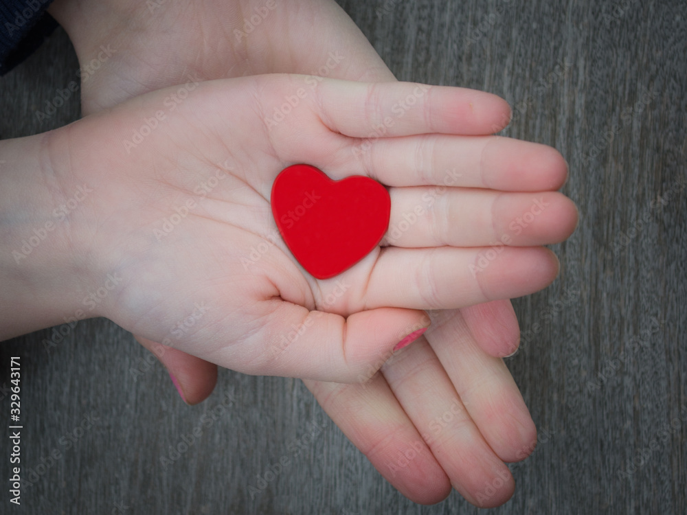 Fototapeta premium Two kids holding red heart in hand over solid wooden background in a conceptual image of love, family and care.