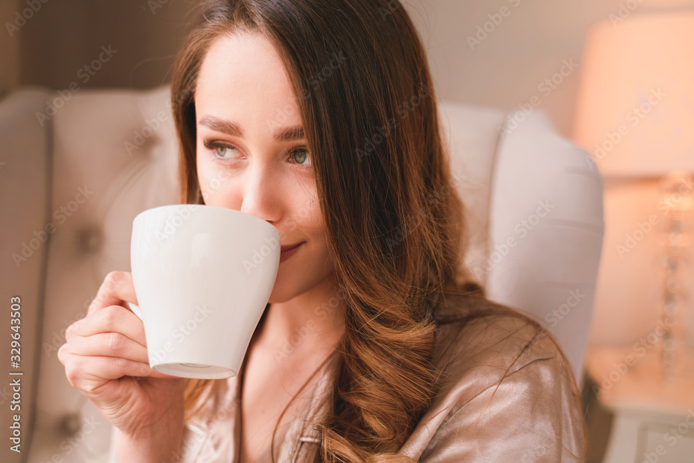 Sensitive young woman delights morning. Meeting sunrise, enjoyment and calmness concept, positive beginning of day. Lady has long blonde wavy hair, beautiful smile. Wearing nice fashionable pajama.
