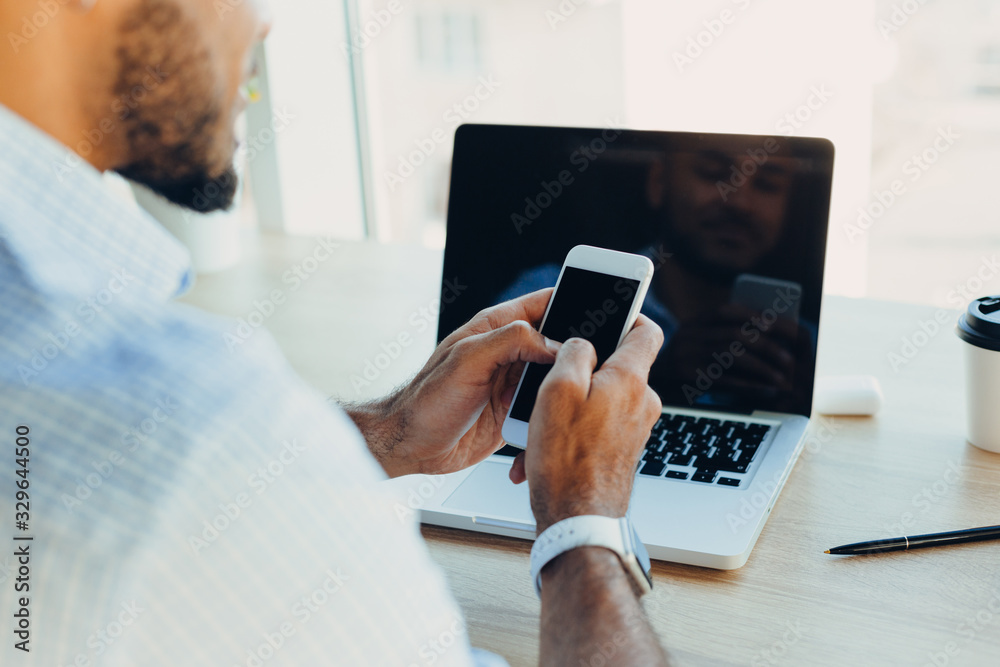 Confident young african american businessman working on laptop and talking on a cell phone while sitting at his workplace in startup office Confident young african american businessman working on laptop and talking on a cell phone while sitting at his workplace in startup office