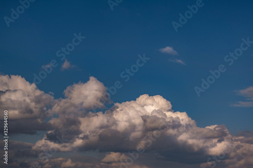 Blue sky background with evening fluffy curly rolling clouds. Good windy weather