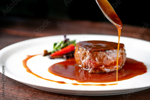 Grilled beef tenderloin steak on a white platter is served with demiglas sauce photo