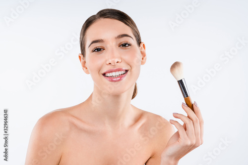 Beauty portrait of young smiling woman holding make up brush isolated over white background