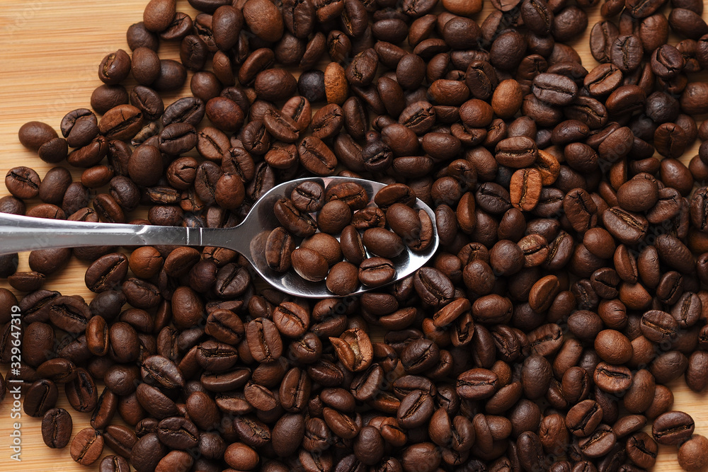 a handful of coffee beans on a wooden background with a metal spoon in the center