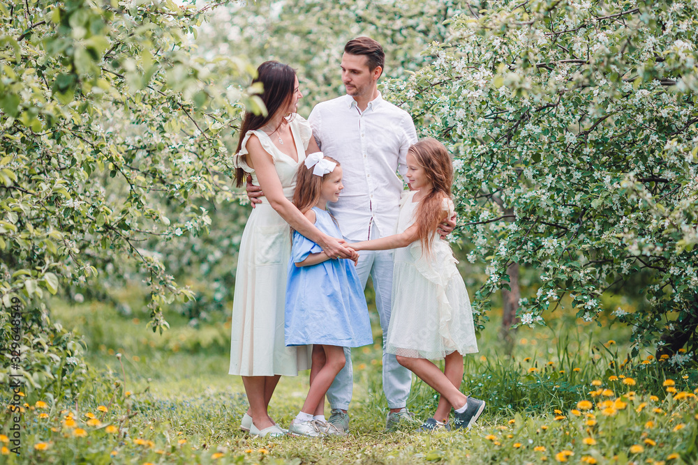 Adorable family in blooming cherry garden on beautiful spring day