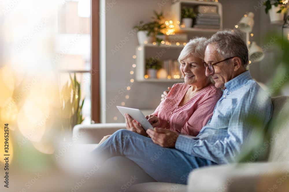 Mature couple using a laptop while relaxing at home - obrazy, fototapety, plakaty 