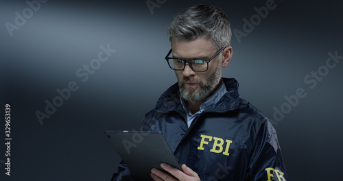 Good looking Caucasian grey-haired male FBI policeman in glasses tapping and scrolling on the tablet device while browsing. photo