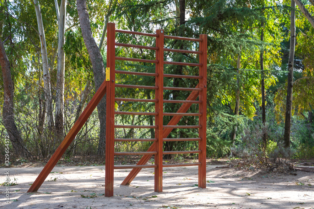 Fototapeta premium View of wooden apparatus for training in a sports area of a park with trees, in Madrid, Spain. Horizontal