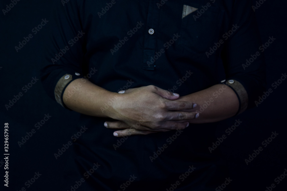 Young man praying with arms across posture. Islamic praying concept on black background. Selective focus on finger