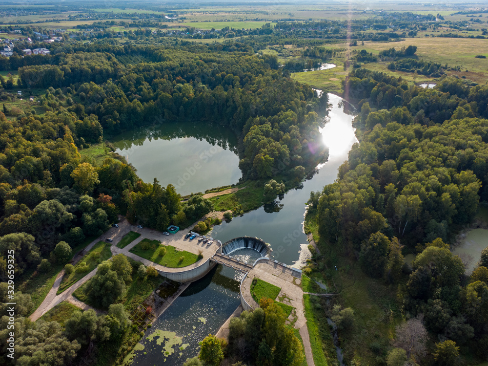 Aerial photo of a hydroelectric power station in the country, a bridge and a funnel in the water, in the frame a lake and nature, the sun is reflected in the water