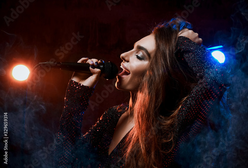 Beautiful singing girl curly afro hairstyle. Beauty woman singer sing with microphone karaoke song on stage in dark background photo