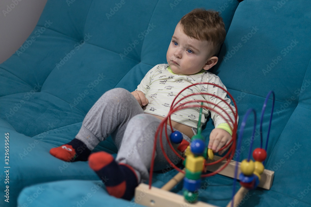 Obraz premium childhood development. happy child with a colored educational toy. the kid is playing a finger maze. a child is playing on a blue sofa.
