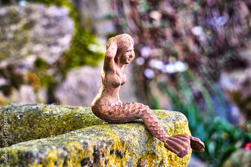 Sculpture of a little mermaid on a natural stone as a garden decoration.