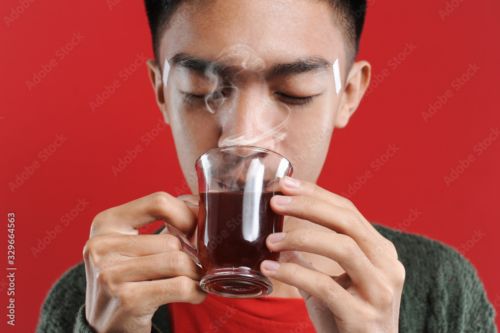 Sick cold and headache Young Asian man wearing a sweater while drinking hot tea
