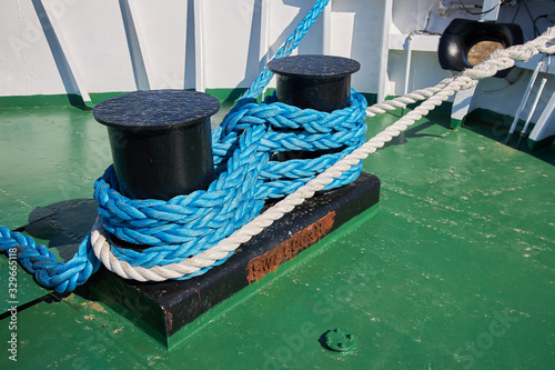 Fotografie Powerful bollard on the ship fore deck is tied with white and blue nylon ropes