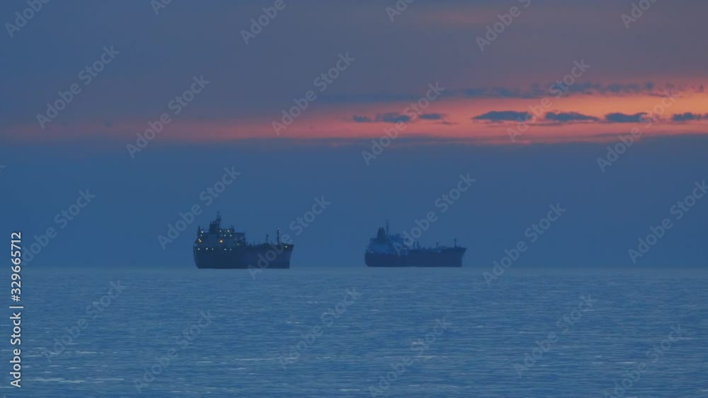 Steady shot of a two cargo ships sailing in an ocean without waves near port in Portugal. Sunrise and dark clouds in the background. Steady shot of a two cargo ships sailing in an ocean without waves near port in Portugal. Sunrise and dark clouds in the background.