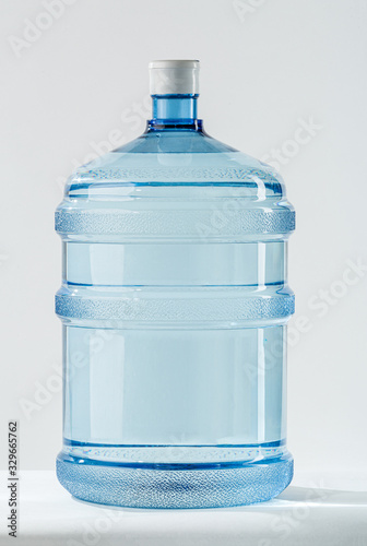 Big Blue Transparent Pet plastic water bottle for the cooler. 19 liter or 5 gallon refillable plastic water BPA Free jug dispenser. Mineral water delivery for offices. Studio shot on white background.