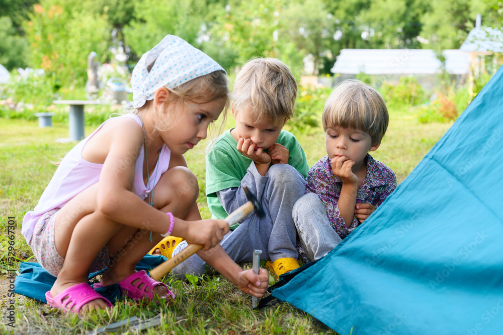 cute little boys and girl toddlers help set up a camping tent. family with little children have fun spending summer holidays in nature outdoor - obrazy, fototapety, plakaty 