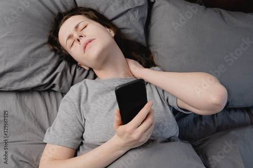 Fibromyalgia concept. Top view of unhappy young woman lying in bed in morning feels pain in neck after sleep, massage tense neck muscles, exhausted upset girl suffering from shoulder ache. photo