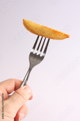 A studio photograph of a cooked oven chip on a fork