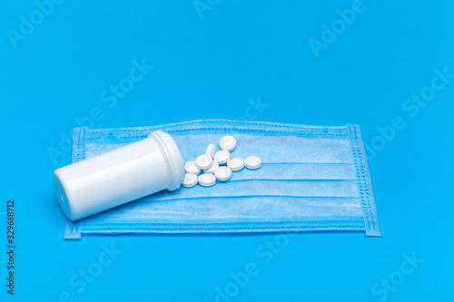 medical mask with a bottle of a medicinal product with a scattered pile of pills for the treatment of the respiratory tract of the lungs on a blue background with copy space.