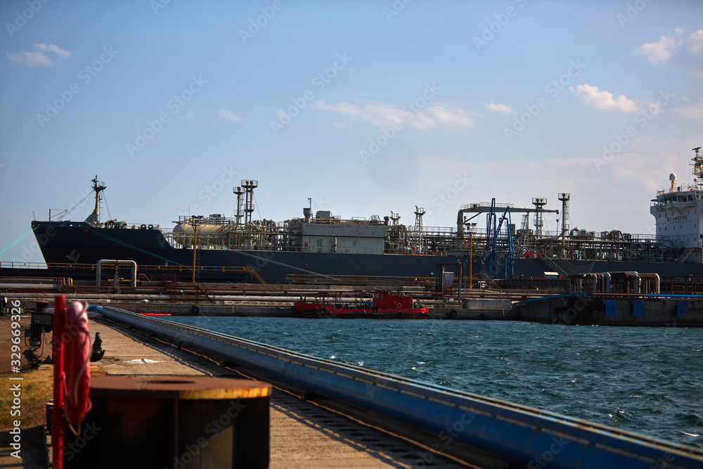 Fototapeta premium merchant vessel is gas carrier at port log terminal. The tanker at the terminal of the industrial port loads with gas, unloads the gas.