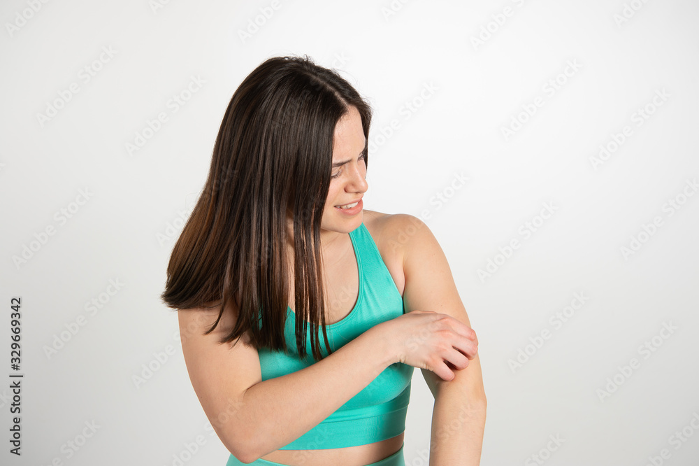 Nice brown haired girl scratching her arm, it itches her. Emotional expression of female athlete model isolated over white background. Active and healthy lifestyle, emotions concept... Nice brown haired girl scratching her arm, it itches her. Emotional expression of female athlete model isolated over white background. Active and healthy lifestyle, emotions concept...