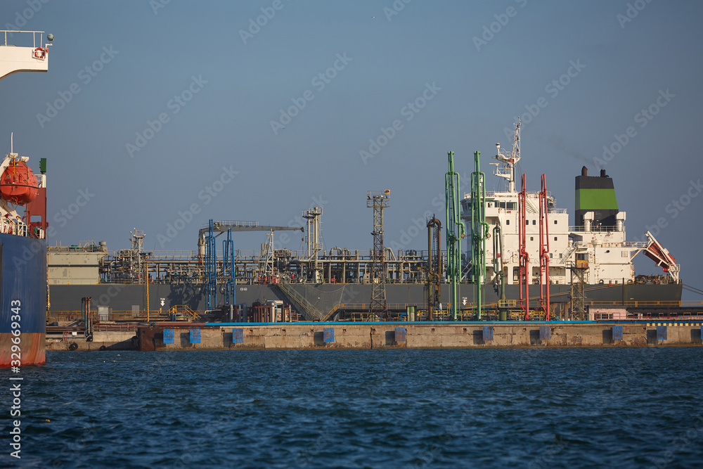 merchant vessel is gas carrier at port log terminal. The tanker at the terminal of the industrial port loads with gas, unloads the gas. merchant vessel is gas carrier at port log terminal. The tanker at the terminal of the industrial port loads with gas, unloads the gas.