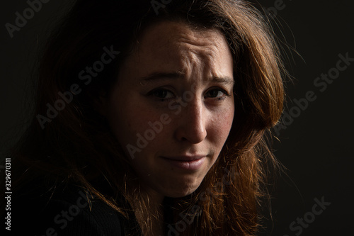 Low key portrait of sad brunette girl looking at camera against black background. Emotions in female face...