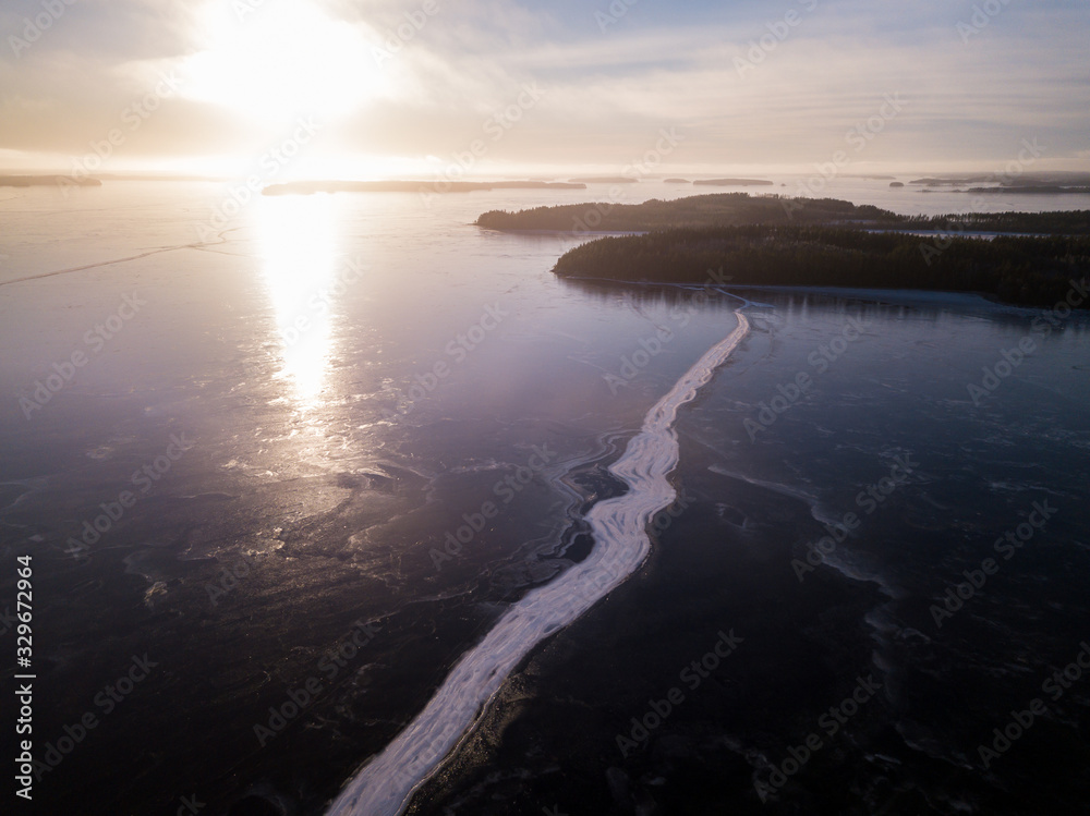 Wide crack on ice cover at frozen lake during sunset