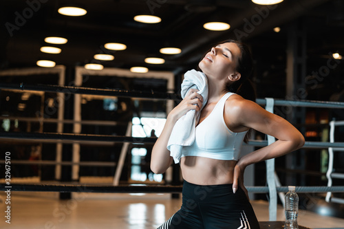 Smiling fit girl holding towel and taking rest in gym. Girl wipes sweat with a towel